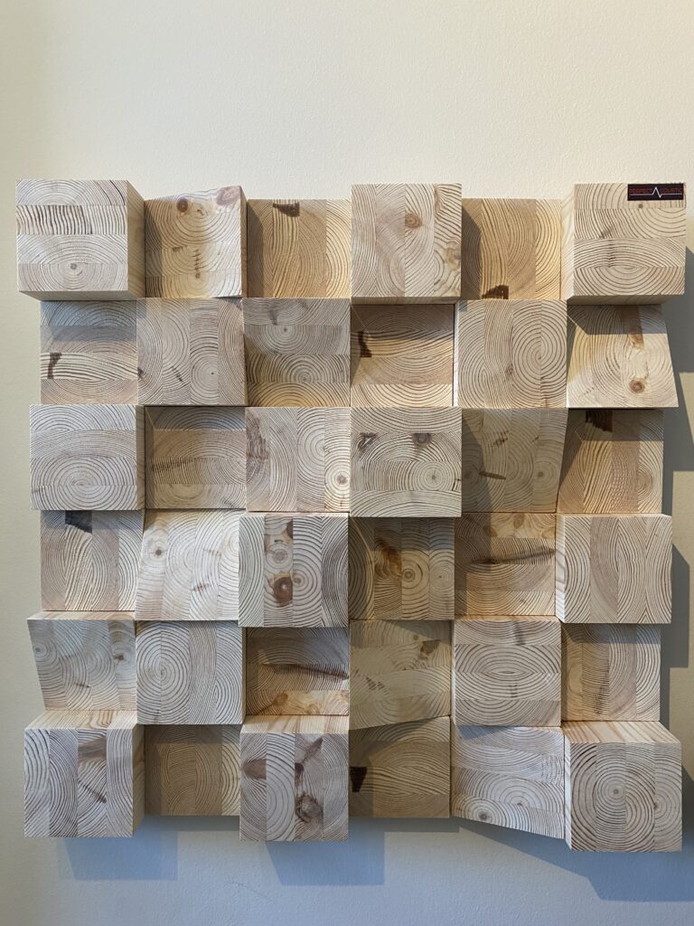 Diffusori Skyline 60x60x14 cm in una sala d’ascolto moderna, con struttura tridimensionale in legno dietro l’impianto hi-fi