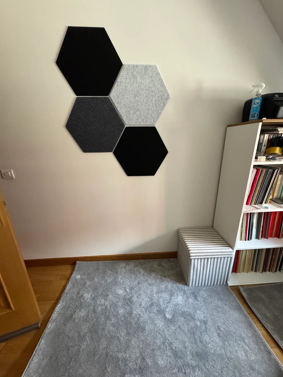 Composizione minimale di pannelli esagonali Bilnora in feltro nero, grigio scuro e grigio chiaro applicati su una parete chiara.
