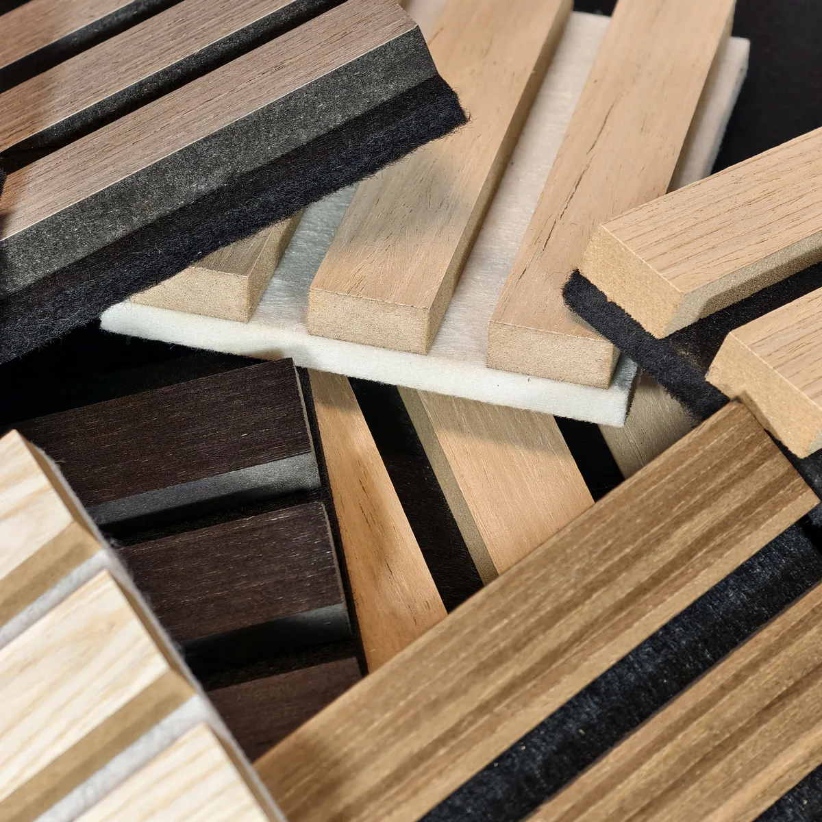 Composizione di campioni del pannello fonoisolante Freja in legno con diverse finiture, lamelle smontate e retro in feltro nero, utile per osservare spessori, texture e struttura del materiale.