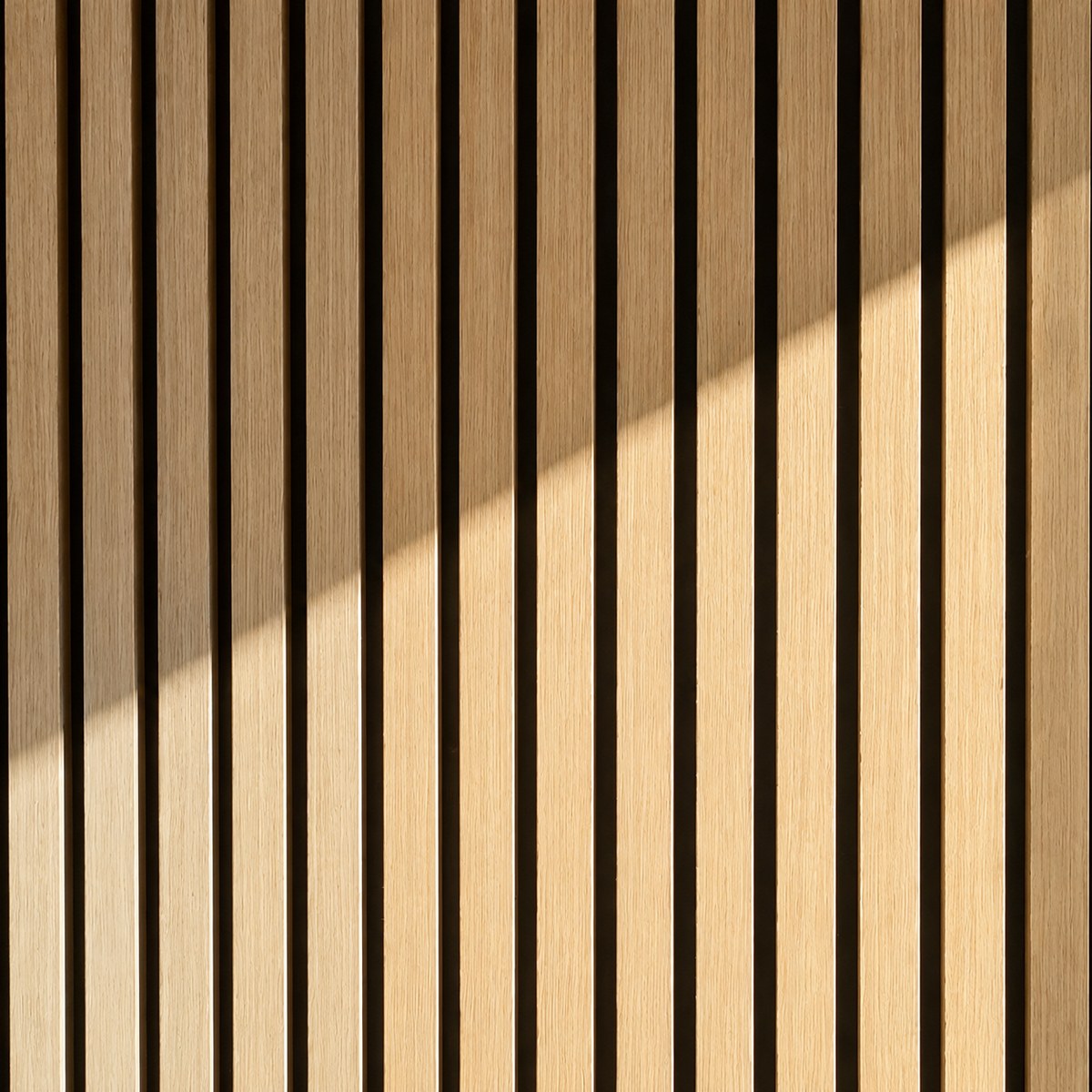 Dettaglio ravvicinato di un pannello fonoisolante Freja in legno con lamelle verticali in rovere chiaro e fondo nero a contrasto, attraversato da una luce diagonale che ne valorizza la texture.