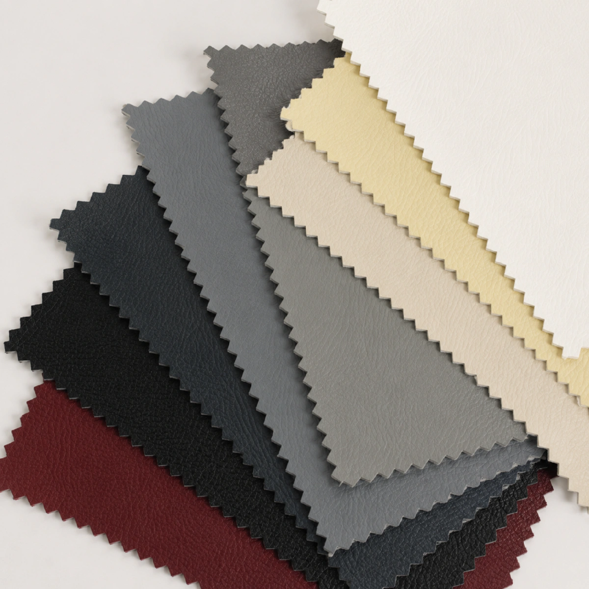 Campioni di similpelle Polo al metro sovrapposti in diverse tonalità, tra cui bianco, crema, grigio, antracite, nero e bordeaux, con superficie leggermente testurizzata.
