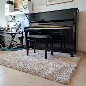 tappeto-acustico-professional-calm-beige-stanza-musica Tappeto acustico Professional Calm beige collocato in una stanza musica sotto un pianoforte, con superficie spessa e texture shaggy ben visibile.